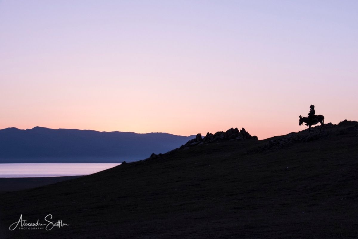 Femme à cheval face au lac Son-Kul pendant le coucher du soleil, Kirghizistan