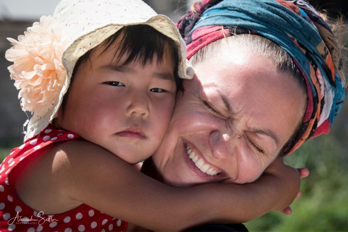 Voyage chez l'habitant Kirghizistan : petite fille kirghize dans les bras d'une voyageuse